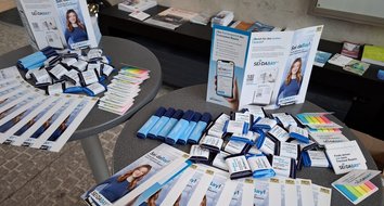 Flyer und Give-Aways an der TH Augsburg Auf einem Stehtisch liegen Flyer, Schokolade, Textmarker und Heftnotizen im Sei-daBay-Design.