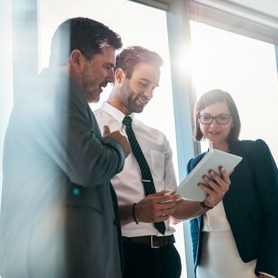 Drei Geschäftsleute stehen vor einem Fenster und betrachten ein Tablet. Drei Geschäftsleute stehen vor einem Fenster und betrachten ein Tablet.