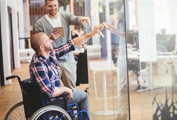 Ein Mann im Rollstuhl zeigt auf eine Glaswand. Ein Mann im Rollstuhl zeigt auf eine Glaswand.