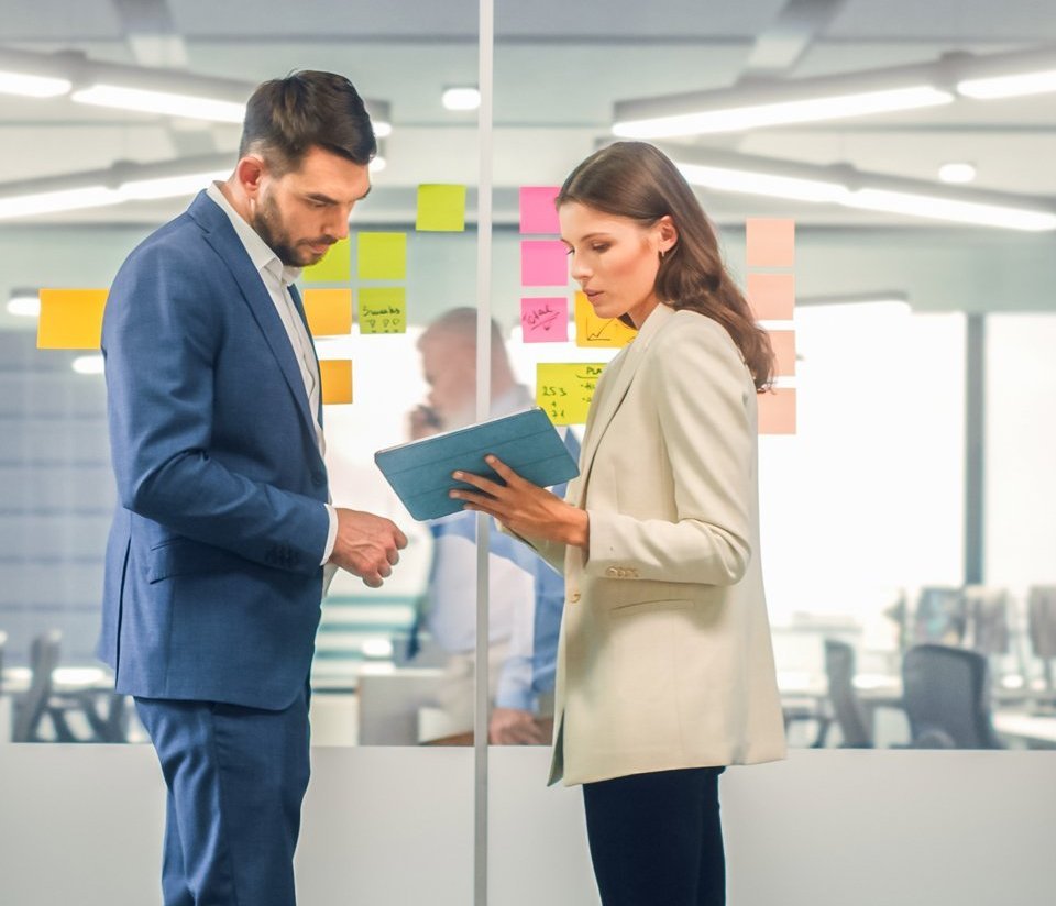 Eine Frau und ein Mann stehen vor einer Glasscheibe und unterhalten sich.