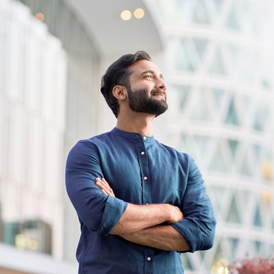 Ein bärtiger Mann mit blauem Hemd steht vor einem modernen Gebäude. Ein bärtiger Mann mit blauem Hemd steht vor einem modernen Gebäude.