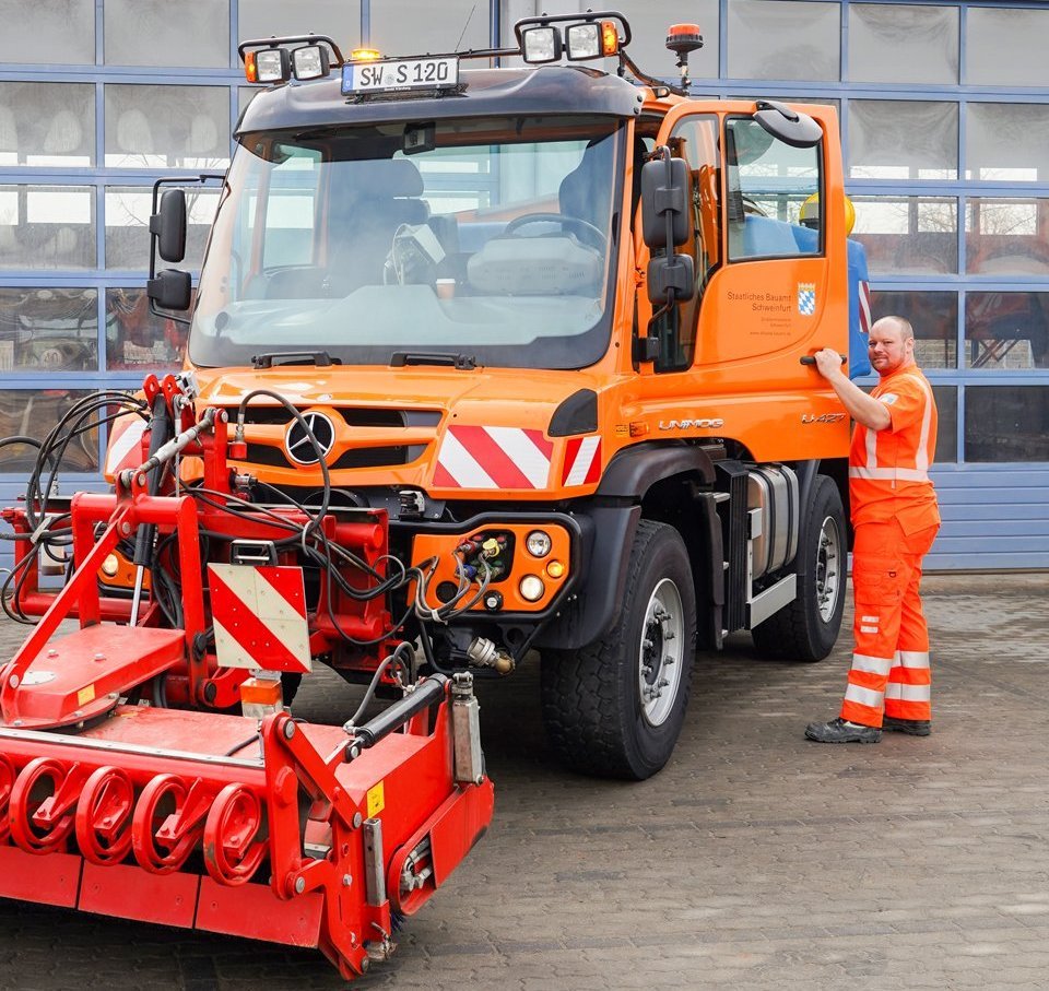 Eine Person steht neben einem Baustellenfahrzeug.
