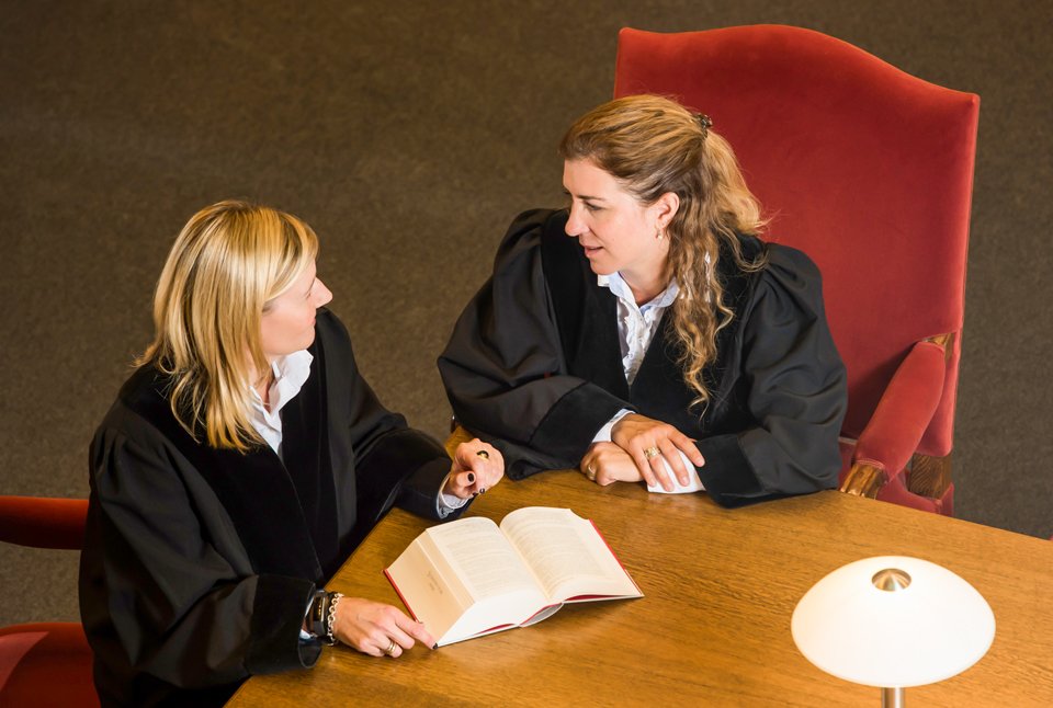 © Bayerisches Staatsministerium der Justiz Zwei Frauen in Richtergewand sitzen an einem Tisch und unterhalten sich.