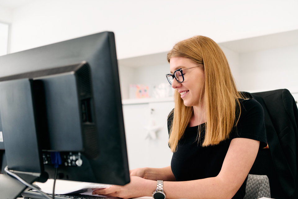 Frau mit langen Haaren und Brille arbeitet an einem PC 