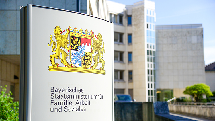 © Bayerischen StMAS Schild für das Bayerische Staatsministerium für Familie, Arbeit und Soziales im Vordergrund des Gebäudes.
