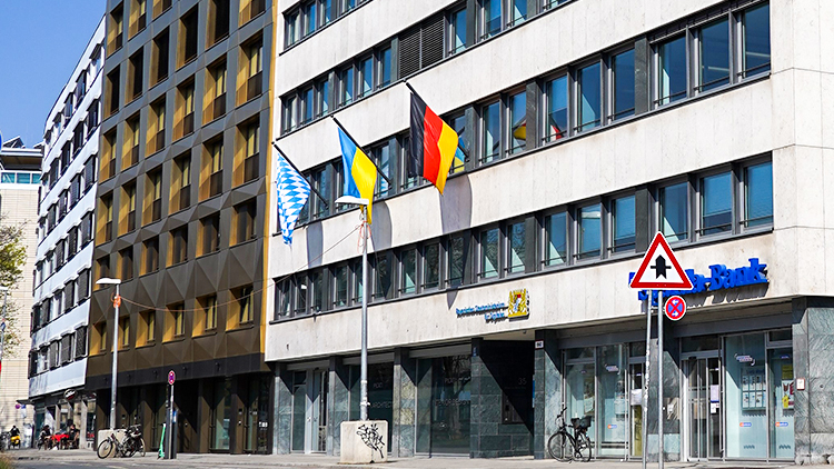 © Bayerischen Staatsministerium für Digitales Bürogebäude mit Deutschland-, Bayern- und Ukraine-Flagge.